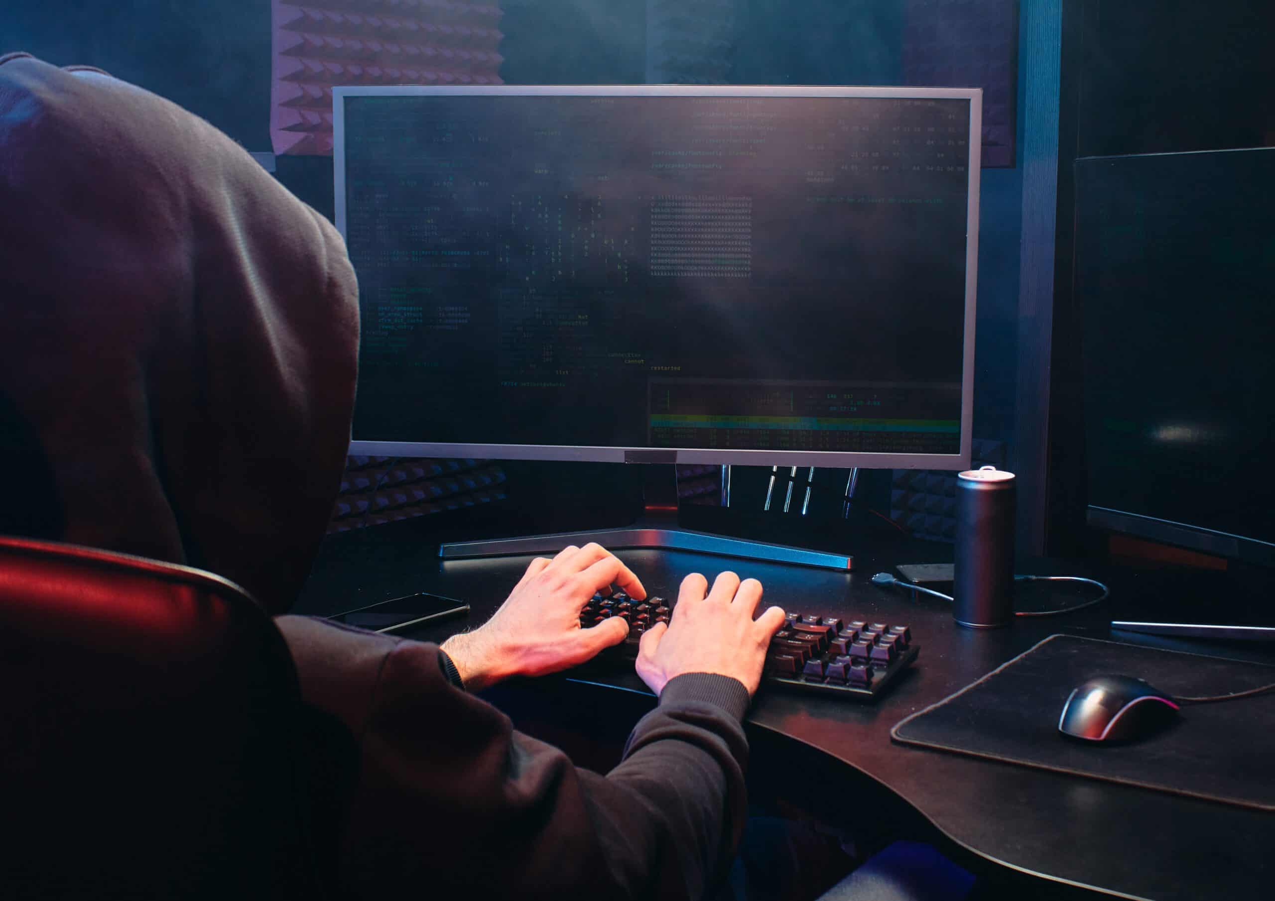 Mężczyzna siedzący tyłem w kapturze przed komputerem najprawdopodobniej wykradający dane osobowe - kradzież dowodu osobistego